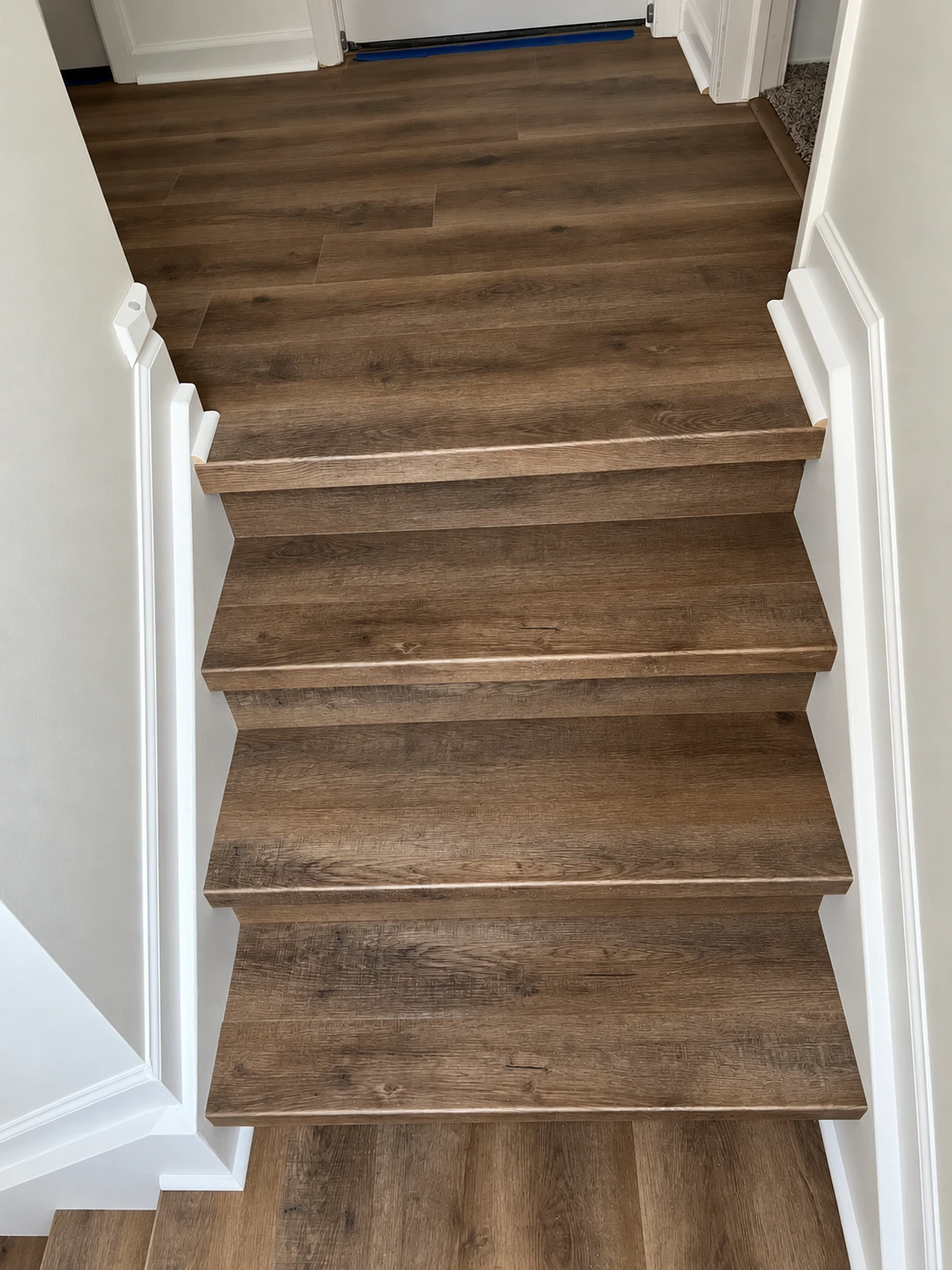 Brown wood-look vinyl stair treads leading to a matching upper landing